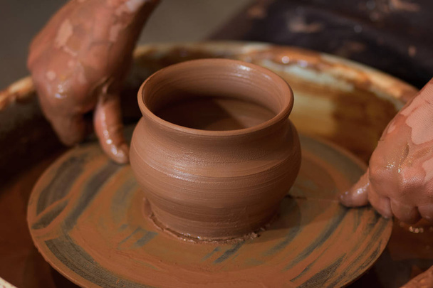 Roterende Potters wiel en klei aardewerk daarop genomen van bovenaf. A beeldhouwt zijn handen met een klei-cup op een potter van wiel. Handen in de klei.  - Foto, afbeelding
