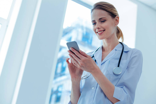 Delighted doctor using her smartphone - Zdjęcie, obraz