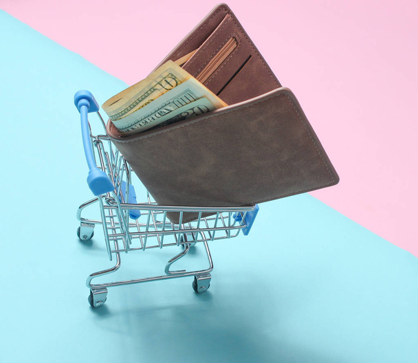 色のパステル調の背景、消費者の概念、ミニマリズム、トップビューのショッピングのためのミニショッピングトロリーでお金を持つ財布 - 写真・画像