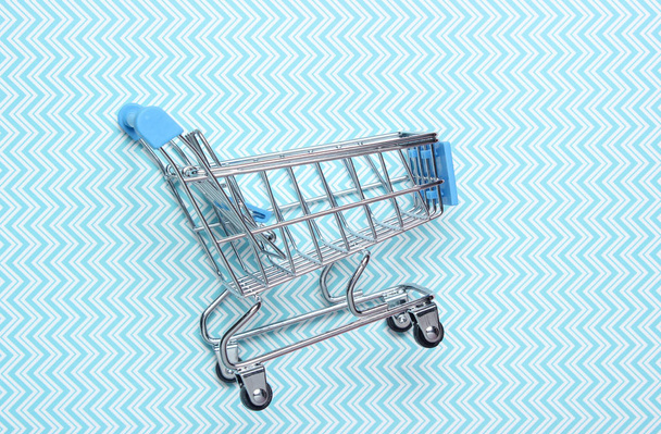 Мини-торговый тролли для покупок на синем фоне, потребительская концепция, минимализм, вид сверху
 - Фото, изображение