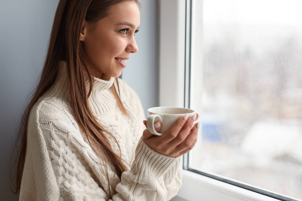 Smiling woman with hot coffee near window - Photo, Image