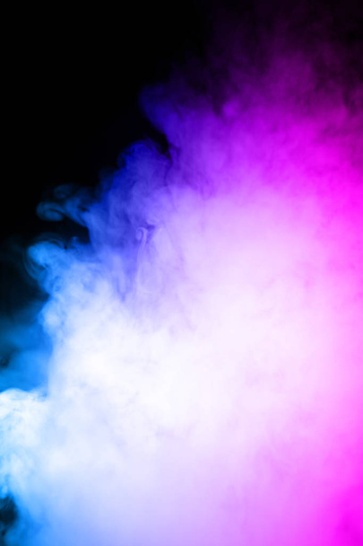Mężczyzna trzyma vape w gęstej wapiennej mgle lub dymie. Vape chmury wokół strony z vape na czarnym tle. Mgła jest podwójny kolor niebieski i fioletowy. Zasoby pojedynczy kolorowy dym z rozpylaną gliceryną. - Zdjęcie, obraz