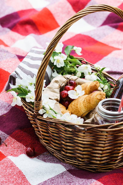Picnic basket with food and flowers on red blanket. - Фото, изображение