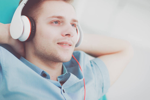 A young handsome man on the couch listening to music - Foto, afbeelding
