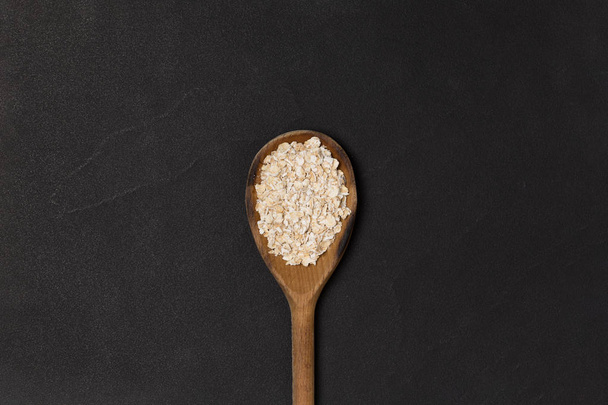 Cucchiaio di legno con farina d'avena / porridge / avena su piatto nero con spazio copia. Vista dall'alto
 - Foto, immagini