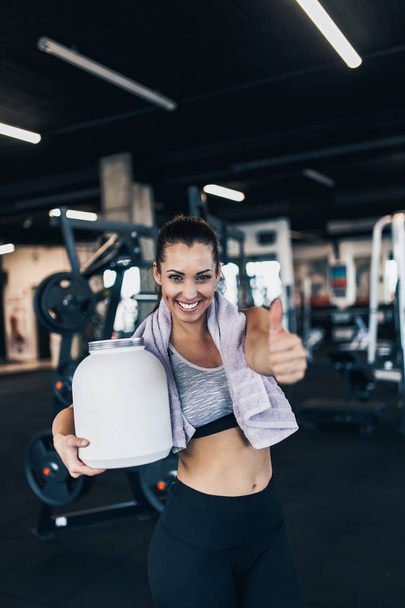Young attractive woman after successful workout posing and smiling in modern fitness gym while showing thumb up - Foto, immagini