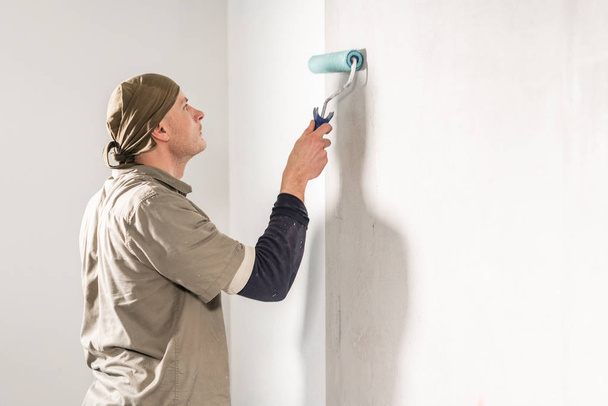 Young man, worker glueing wallpapers on concrete wall. Repair the apartment. Home renovation concept. White Wallpaper for paint - Fotoğraf, Görsel