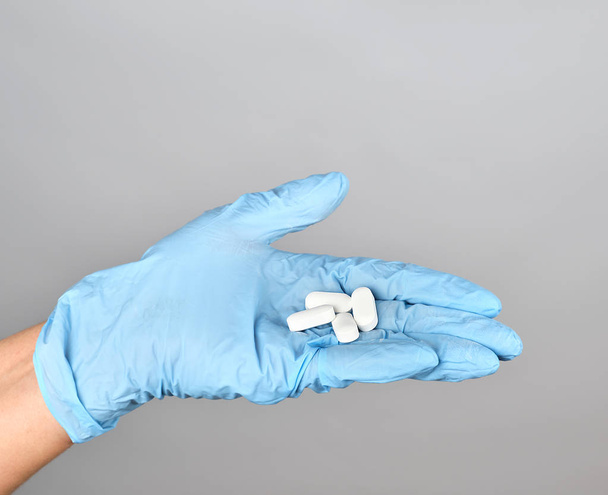 modrá sterilní ruka v rukavicích držící bílé prášky  - Fotografie, Obrázek