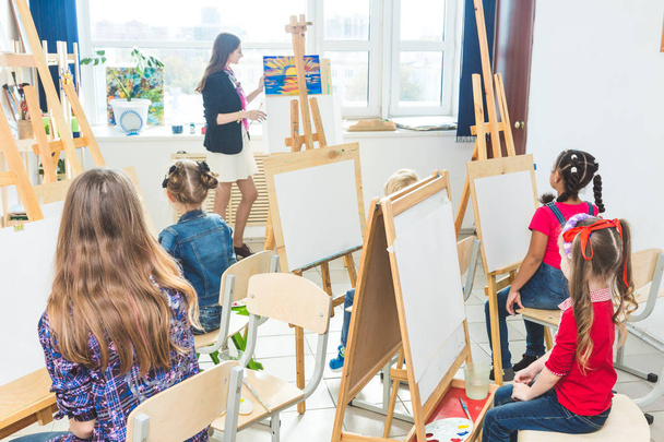 A group of preschool students and young teacher in drawing class paint in gouache. mixed race schoolgirl afroamerican and boy. Artwork - Фото, зображення