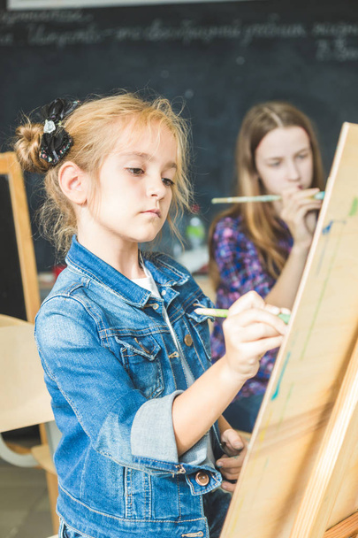 little girl with a teacher in group of preschool student sat the drawing a picture. Painting on maelbert, palette and paints. Back to school and Education concept. - Fotografie, Obrázek