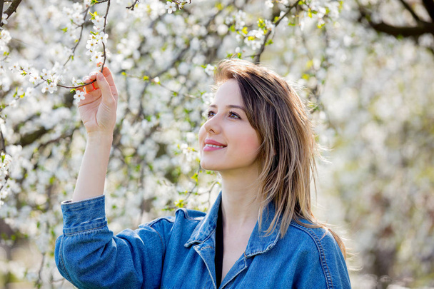 girl in a denim jacket stay near a flowering tree - Foto, afbeelding