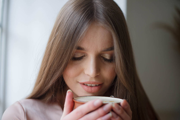 Beautiful girl is drinking coffee and smiling while sitting at the cafe - Foto, imagen