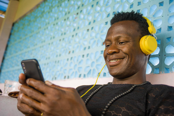lifestyle portrait of young attractive and happy cool hipster black afro American man using mobile phone and headset networking on internet social media app  - Zdjęcie, obraz