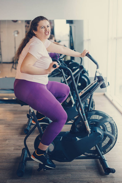Fat woman intensely exercising on stationary bike - Foto, afbeelding