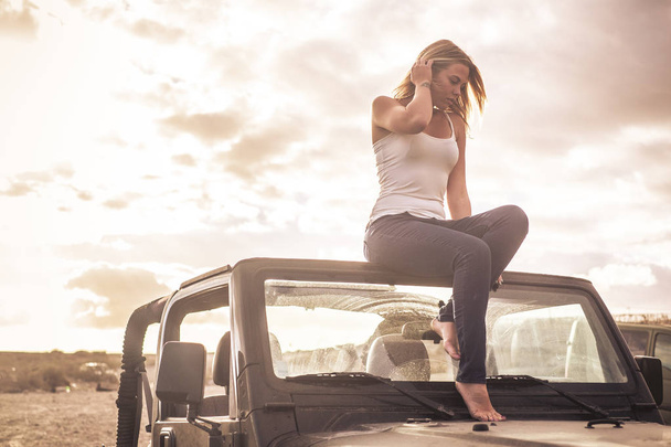 Thoughtful jovencita rubia guapa sentada en su coche convertible con pies desnudos. - Foto, imagen