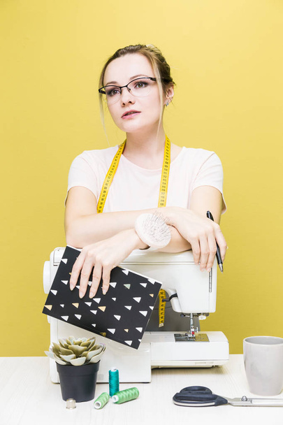 Sewing workshop. Seamstress at work. Portrait of a young dressmaker with notebook on a colored background. - Photo, image