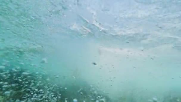 Podwodne Slow Motion: nierozpoznawalny surfer jazdy leżącego na jego deski surfingowej przez pęcherzyki powietrza wypełnione oceanu w słoneczny dzień. Ekstremalnych miłośników sportu korzystających surfing wakacje na Wyspach Kanaryjskich. - Materiał filmowy, wideo