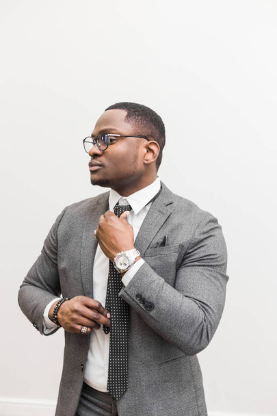 Biznesmen młody Afroamerykanin w szary garnitur, wiązanie krawata na białym tle. - Zdjęcie, obraz
