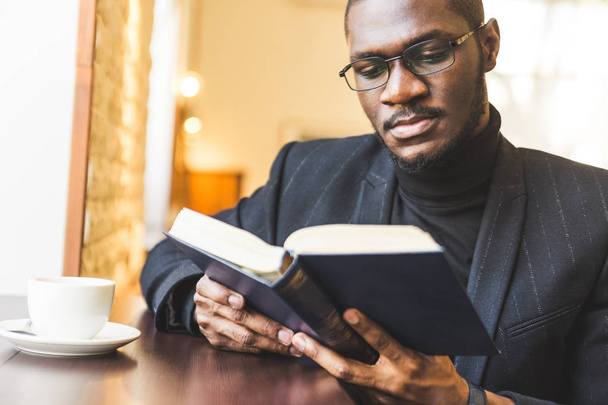 Young handsome dark-skinned businessman in a cafe reads a book with a cup of tea. - Foto, imagen
