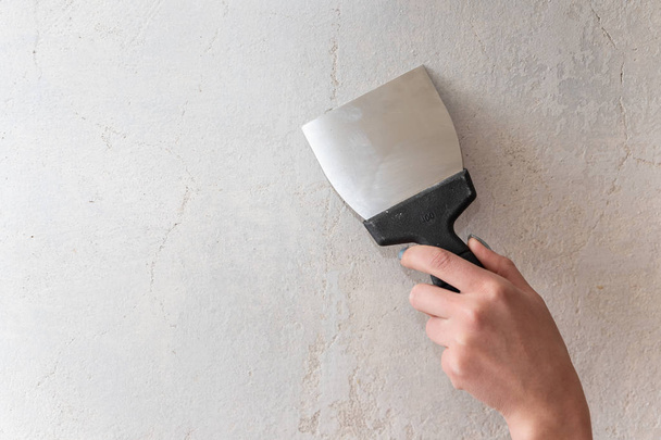 Bir adam elinde bir spatula tutar ve beton duvar boyunca yol açar. Macun düzensizlikleri ve çatlaklar. - Fotoğraf, Görsel