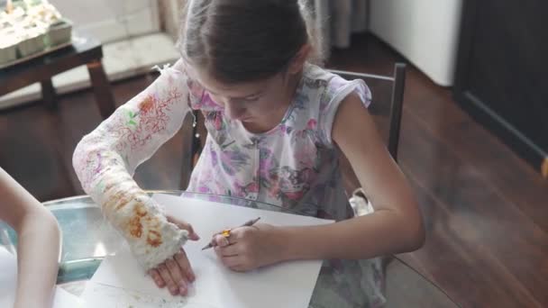Kind mit gebrochenem Arm in Verband zeichnet mit Buntstiften. Kleines Mädchen mit Handverletzung. - Filmmaterial, Video