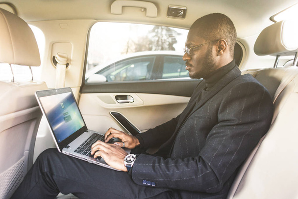 Man in a business suit write on laptop in the salon of an expensive car with leather interior. - 写真・画像