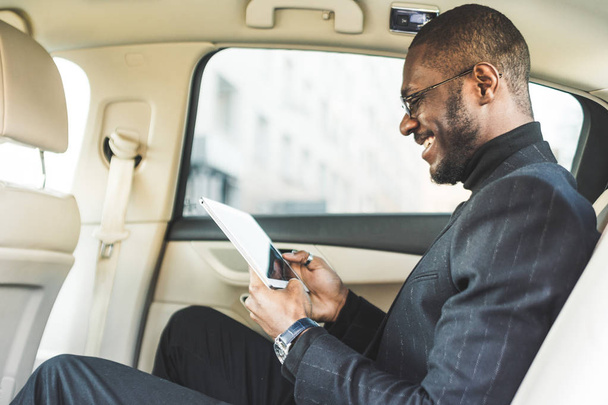 Young businessman using tablet while sitting in the backseat of a car. - Foto, Imagen