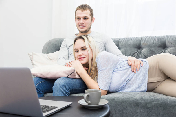 Young beautiful couple resting on the couch and watching online video from a laptop in the living room. - Foto, Bild