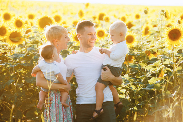 Foto von glücklicher Familie, Eltern und Söhnen, die zusammen im Sonnenblumenfeld lächeln  - Foto, Bild
