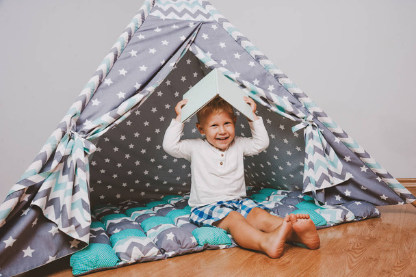 Cheerful and happy kid reading and playing in colorful wigwam  - Photo, image