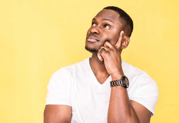 Pensive dark skinned man poses against yellow background. - Фото, изображение