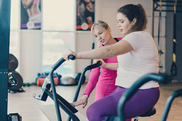 Fat female practicing on stationary bike in fitness club - Foto, Imagen