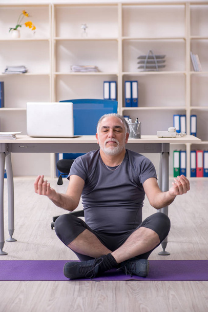Bianco barbuto vecchio dipendente facendo esercizi in ufficio
  - Foto, immagini
