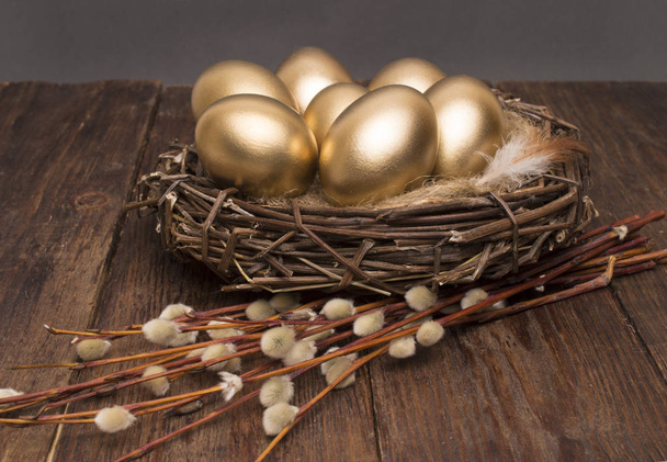 Nest with golden eggs with willow on a wooden background. Easter. - Foto, afbeelding