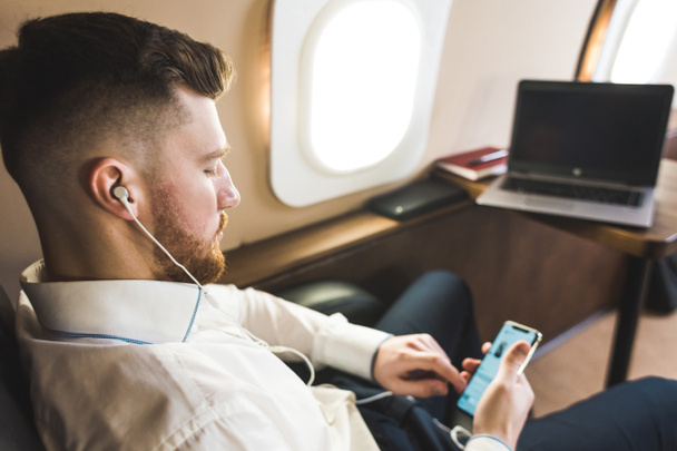 Young attractive and successful businessman is resting and listening to music works while sitting in the chair of his private business plane - Foto, afbeelding