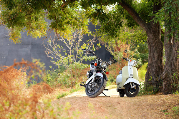 Ročník černá motocykl stojí v blízkosti bílé motorce v paprscích slunečního světla. Boční pohled - Fotografie, Obrázek