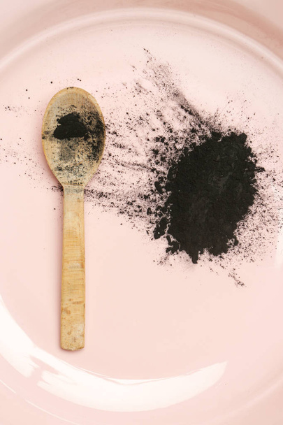 Carbone attivo in polvere in una ciotola con un cucchiaio di legno
 - Foto, immagini