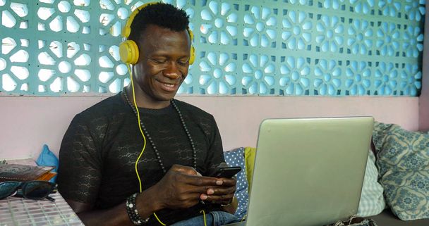 young happy and attractive black African American hipster man networking relaxed with mobile phone and laptop computer smiling in digital nomad job success  - Zdjęcie, obraz