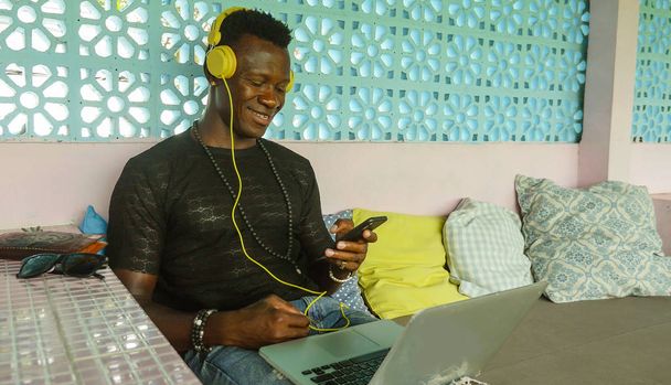 young happy and attractive black African American hipster man networking relaxed with mobile phone and laptop computer smiling in digital nomad job success  - Zdjęcie, obraz