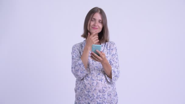 Happy young pregnant woman thinking while using phone - Záběry, video