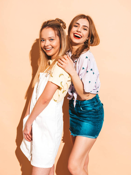 İki genç trendy sarışın hipster kızlarda gülümseyen güzel renkli tişört elbise yaz. Seksi kaygısız kadın bej duvara yakın poz. Olumlu modelleri eğleniyor - Fotoğraf, Görsel