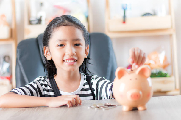 Asian little girl in putting coin in to piggy bank shallow depth - Фото, изображение