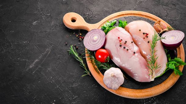 Raw chicken breast with spices and herbs. Barbecue. On a black stone background. Top view. Free copy space. - Photo, image