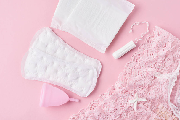 Almohadilla sanitaria, copa menstrual, tampón y bragas sobre fondo rosa
 - Foto, imagen