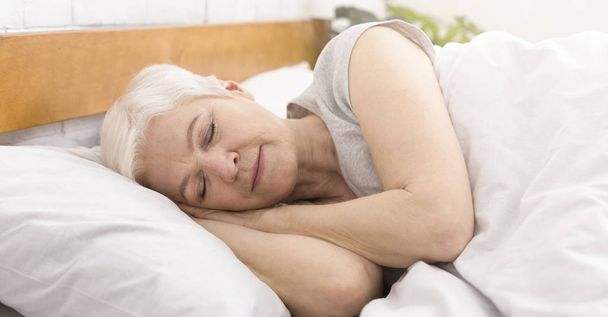 Ηλικιωμένη γυναίκα κοιμάται στο κρεβάτι το πρωί - Φωτογραφία, εικόνα
