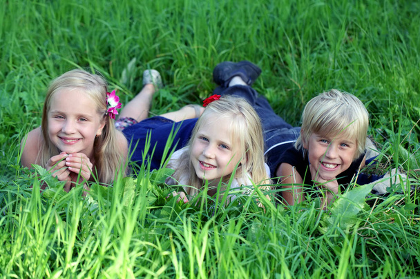 three kids lying on green grass in park - Photo, Image