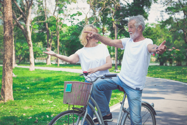 Happy elder couple riding a bicycle in the park - Fotó, kép