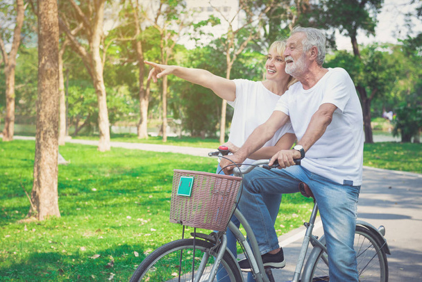 Happy elder couple riding a bicycle in the park - Photo, Image