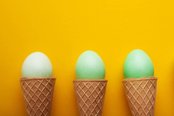 Green easter eggs in waffle cones on yellow background - Foto, Imagem