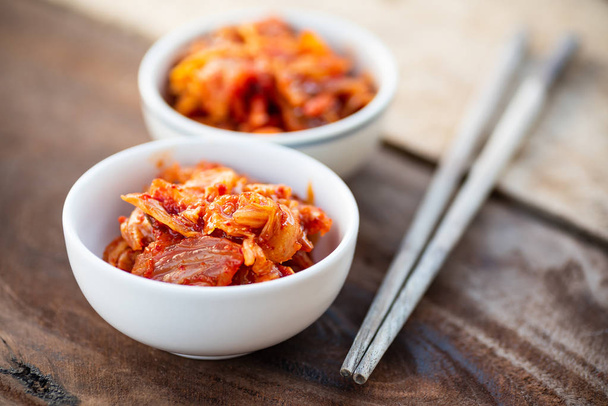 Капуста кимчи в миске с палочками для еды на деревянном столе, корейская еда
 - Фото, изображение